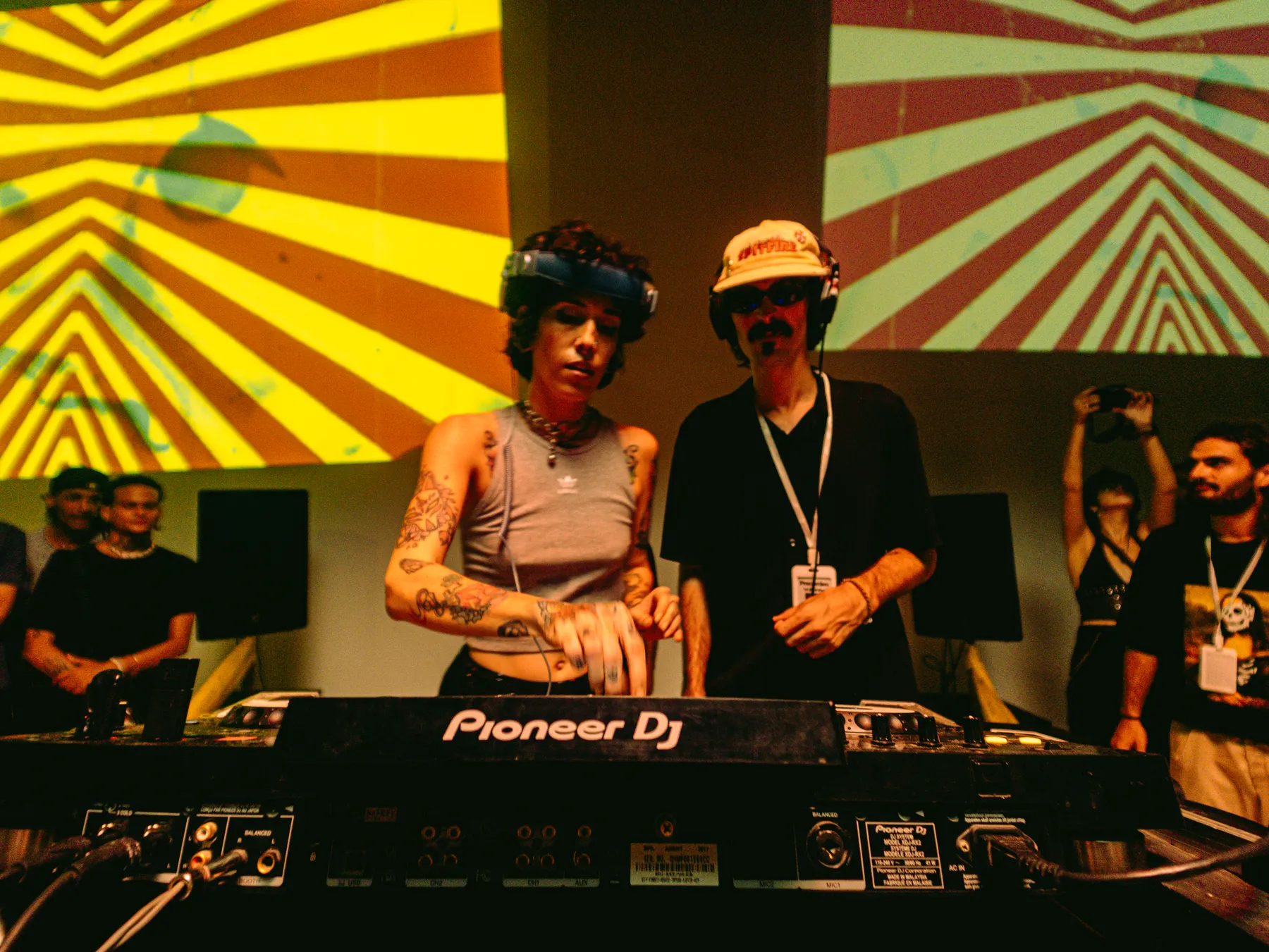 Dos DJ en cabina con visuales amarillos detrás